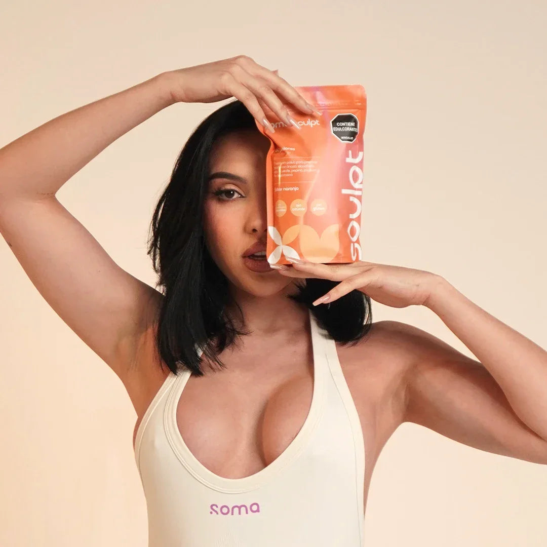 Mujer con top blanco sosteniendo bolsa naranja de SOMA Sculpt sabor naranja, bebida funcional con fibra para saciedad y bienestar digestivo en rutina diaria