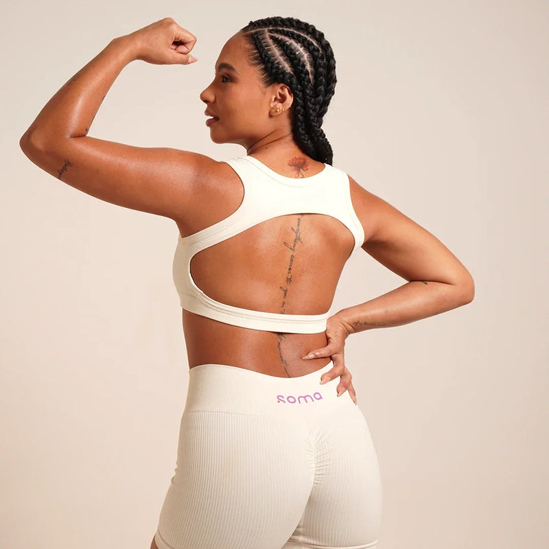 Mujer con sujetador deportivo blanco y leggings Soma, mostrando espalda y bíceps